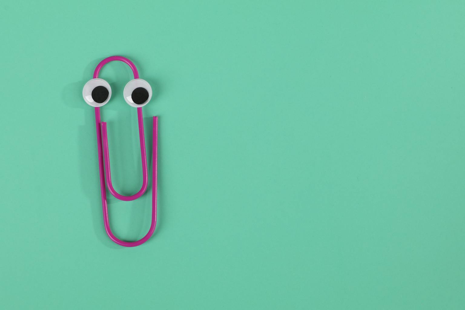 A playful pink paperclip with googly eyes on a green pastel background offers fun visual appeal.