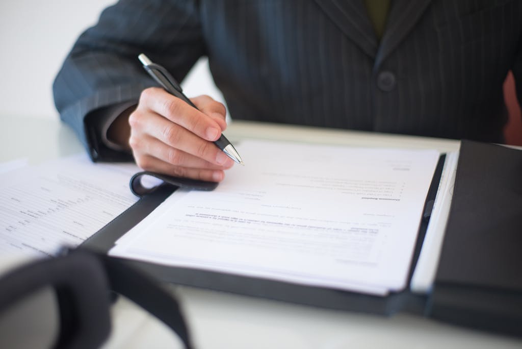 Close-up of a hand signing documents with a pen, symbolizing an important business contract.
